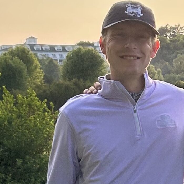 Aaron Holden outdoors on a golf course in a quarter-zip and cap