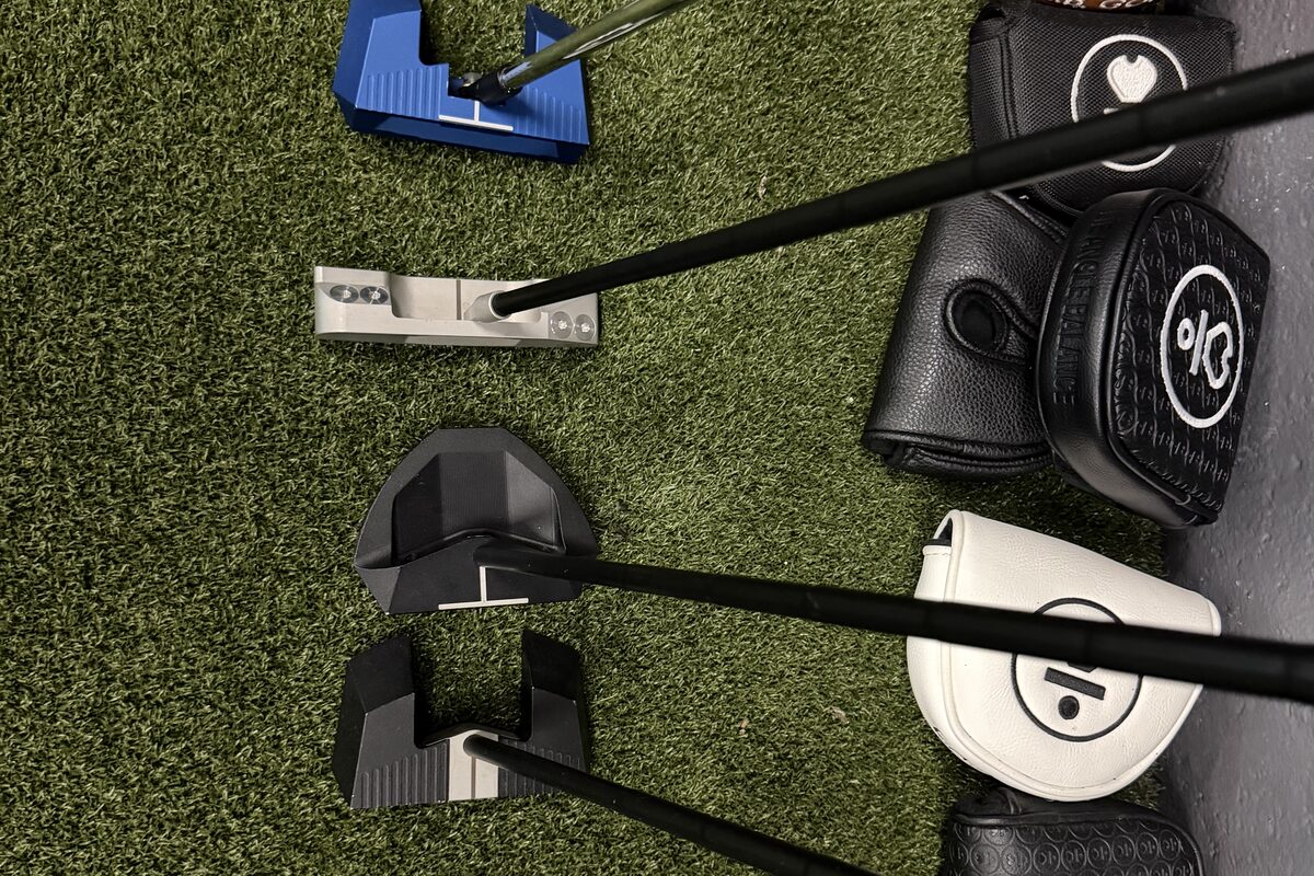 L.A.B. Golf putter heads laid out on the turf beside their headcovers.