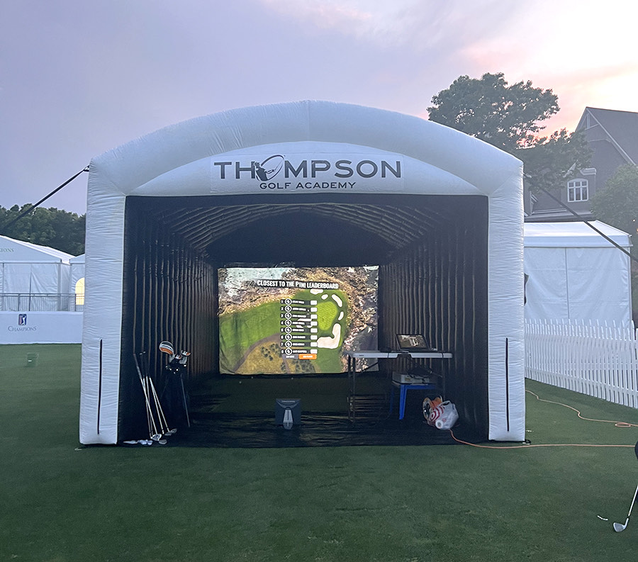 The inflatable golf simulator set up indoors, a golfer mid swing in front of the screen