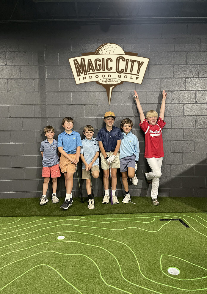 Six juniors with their clubs, standing under the Magic City Indoor Golf sign
                    on the putting green