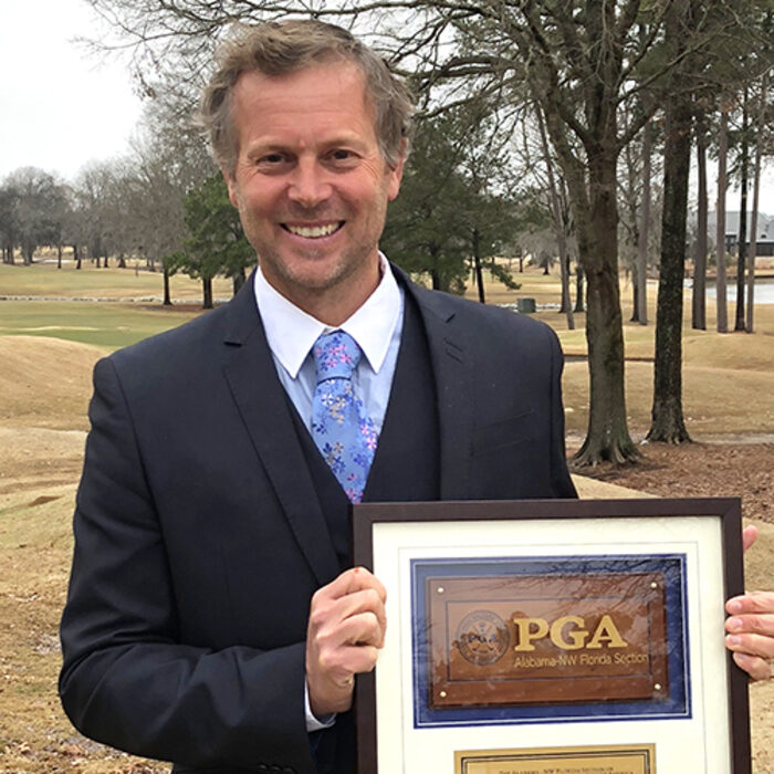Neil Thompson, PGA, outdoors on a golf course holding a PGA section award